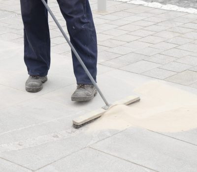 Pavement construction worker filling the block joints with sand using long broom, finishing road paving