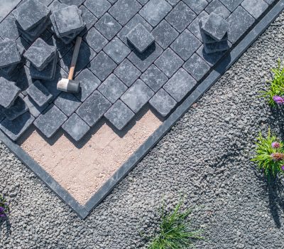 Workers are installing paving stones in a garden pathway, arranging the stones with precision under clear skies.